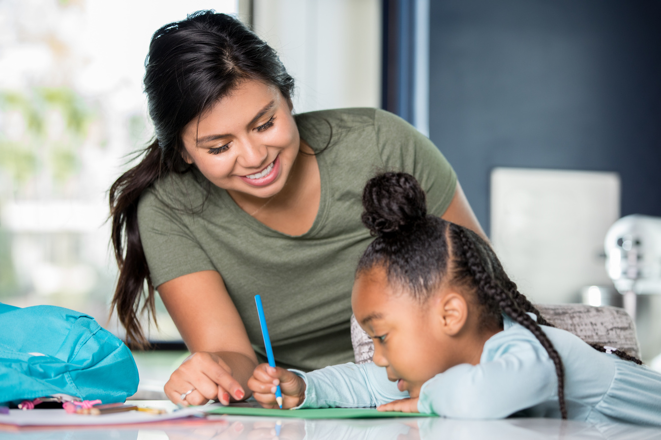 Hispanic young adult woman babysitting child and helping with homework